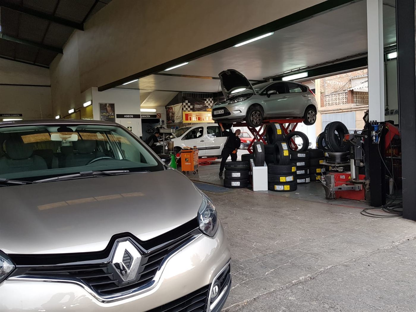 Vista del taller con un coche en el elevador y neumáticos preparados.